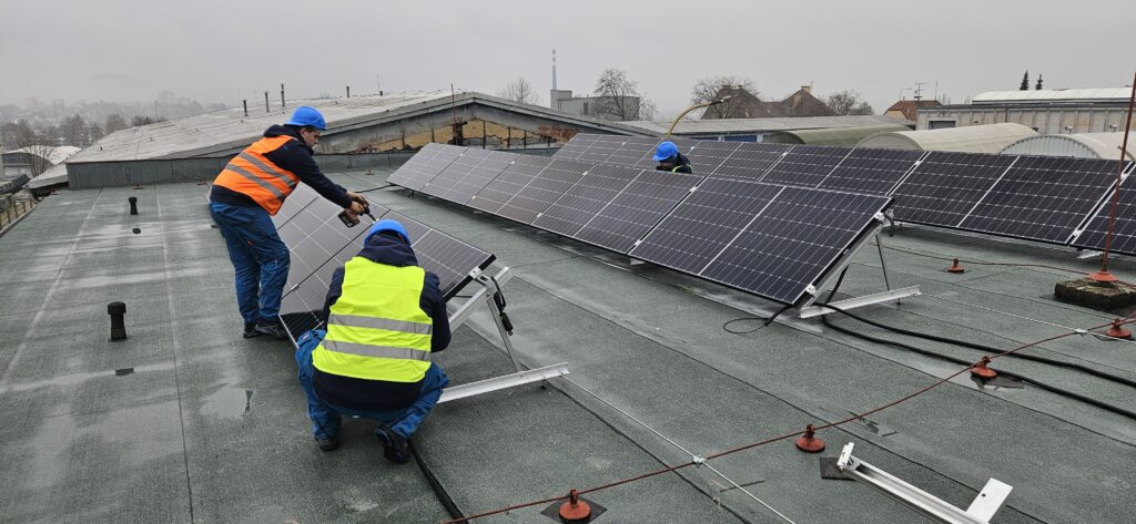 Pracovníci technických služeb na střeše budovy TSM NJ umisťující fotovoltaické panely