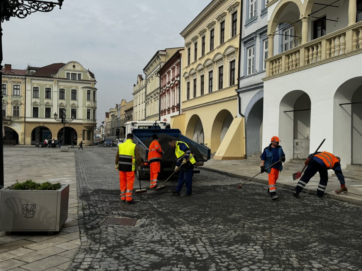 Pracovníci technických služeb rozmetají kameniov do spár žulových kostek