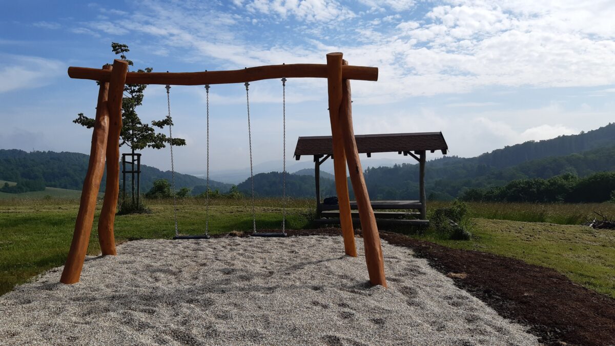 Dvě houpačky a výhled na kopcovitou krajinu.